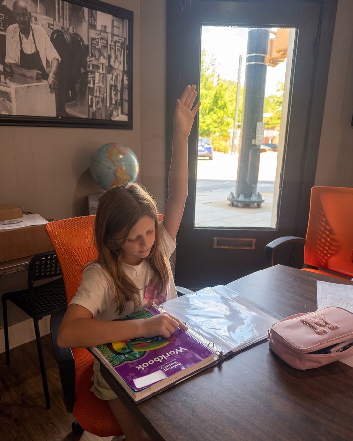 A student raising her hand at the table by the window at Hatch Coworking